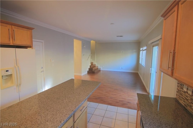 kitchen with light tile patterned floors, white refrigerator with ice dispenser, crown molding, and dark stone counters