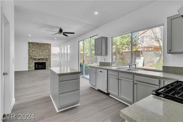 kitchen with gray cabinetry, dishwasher, a stone fireplace, and sink