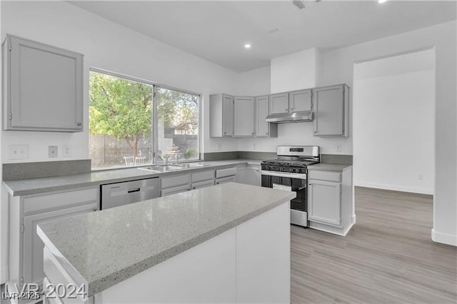 kitchen with a kitchen island, light stone countertops, light wood-type flooring, and stainless steel appliances