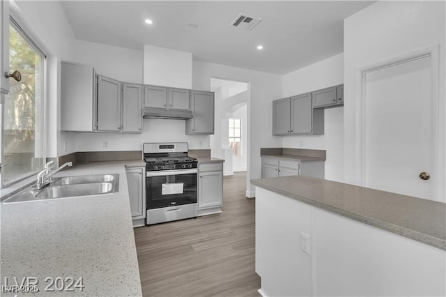 kitchen with gray cabinets, stainless steel range with gas cooktop, sink, and light hardwood / wood-style flooring