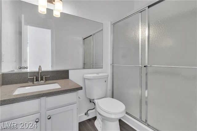 bathroom with hardwood / wood-style floors, vanity, toilet, and a shower with door