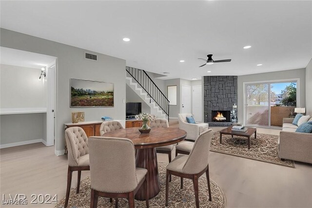 dining area with light hardwood / wood-style floors, a stone fireplace, and ceiling fan