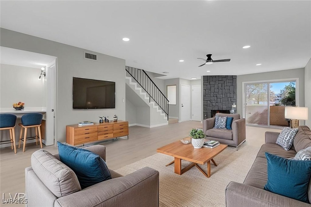 living room featuring ceiling fan, light hardwood / wood-style floors, and a stone fireplace