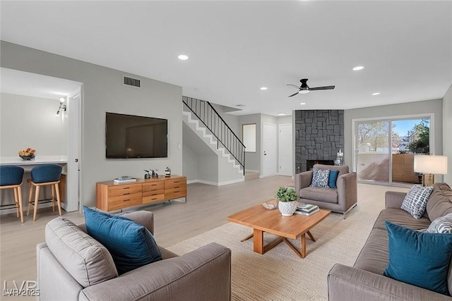 living room featuring ceiling fan, light hardwood / wood-style floors, and a stone fireplace