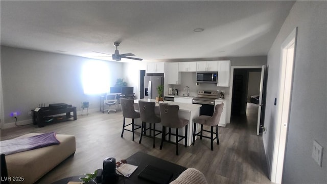 kitchen with a kitchen island, hardwood / wood-style floors, white cabinetry, a kitchen breakfast bar, and stainless steel appliances