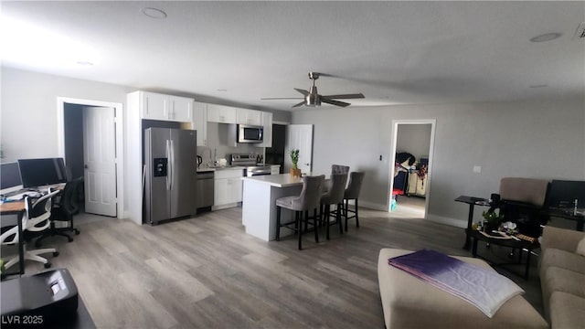 kitchen with appliances with stainless steel finishes, a breakfast bar area, white cabinets, ceiling fan, and light wood-type flooring