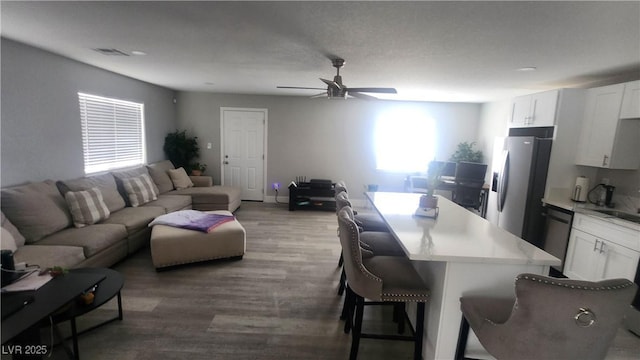 kitchen with white cabinets, a kitchen breakfast bar, ceiling fan, stainless steel appliances, and dark wood-type flooring