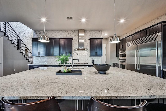 kitchen with pendant lighting, stainless steel appliances, wall chimney exhaust hood, and a spacious island