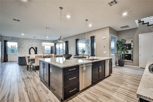 kitchen with light stone countertops, sink, hanging light fixtures, stainless steel dishwasher, and a kitchen island with sink