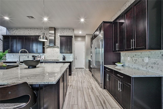 kitchen featuring light stone counters, wall chimney exhaust hood, hanging light fixtures, and light wood-type flooring