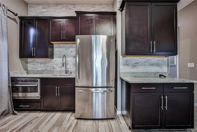 kitchen with dark brown cabinetry, light stone countertops, sink, light hardwood / wood-style flooring, and appliances with stainless steel finishes