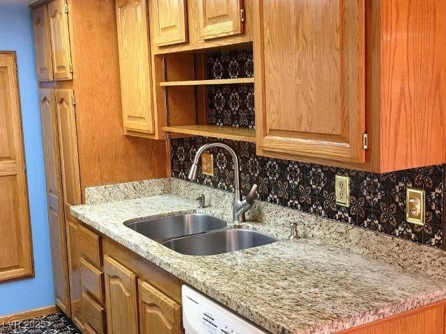 kitchen featuring white dishwasher, light stone counters, tasteful backsplash, and sink