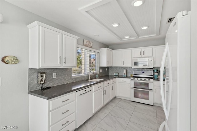 kitchen featuring decorative backsplash, white appliances, a tray ceiling, sink, and white cabinetry