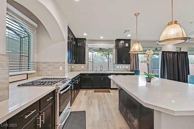 kitchen featuring gas stove, light stone countertops, light hardwood / wood-style flooring, backsplash, and decorative light fixtures