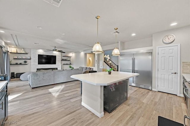 kitchen featuring a center island, stainless steel built in fridge, ceiling fan, decorative light fixtures, and a large fireplace