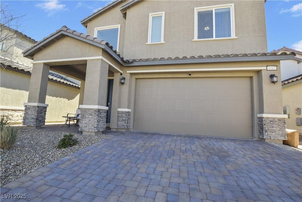 view of front of property featuring an attached garage, stone siding, a tiled roof, decorative driveway, and stucco siding