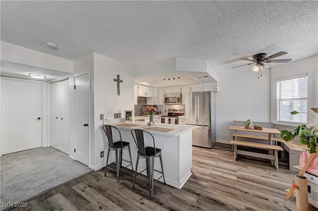 kitchen featuring a kitchen breakfast bar, kitchen peninsula, light wood-type flooring, white cabinetry, and stainless steel appliances