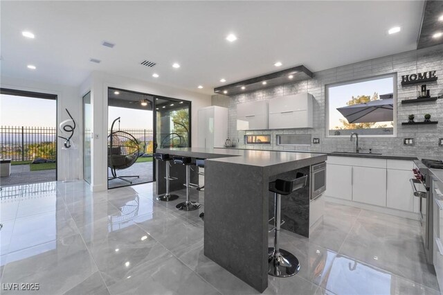 kitchen featuring a kitchen bar, exhaust hood, sink, white cabinets, and a center island