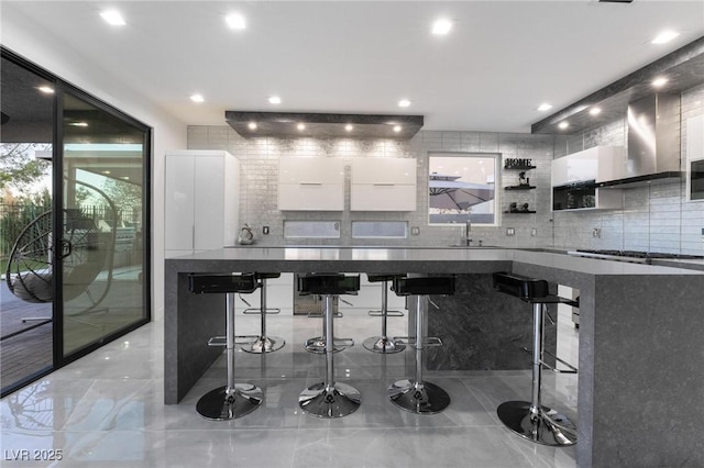 bar featuring stainless steel gas cooktop, sink, white cabinets, decorative backsplash, and wall chimney range hood