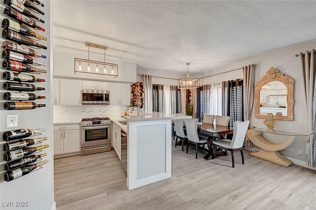 kitchen with appliances with stainless steel finishes, white cabinetry, hanging light fixtures, a notable chandelier, and kitchen peninsula