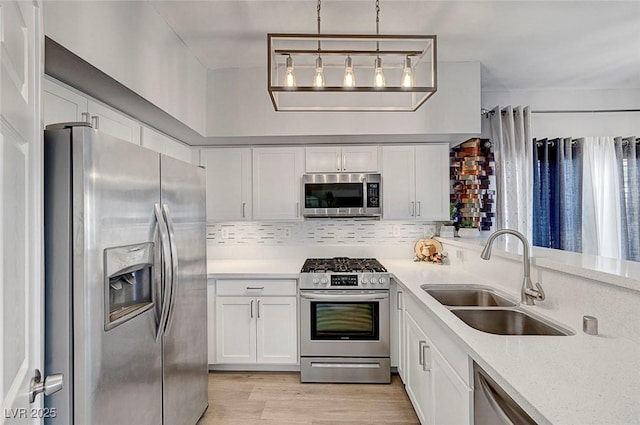 kitchen featuring pendant lighting, sink, stainless steel appliances, light hardwood / wood-style floors, and white cabinets