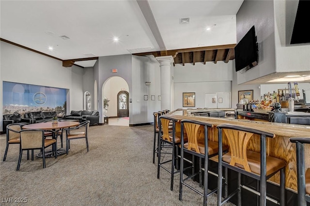 kitchen featuring ornate columns, carpet flooring, beam ceiling, and a breakfast bar