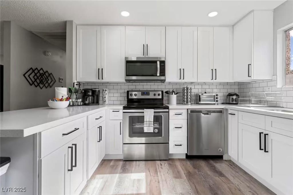 kitchen with white cabinetry, kitchen peninsula, appliances with stainless steel finishes, and tasteful backsplash