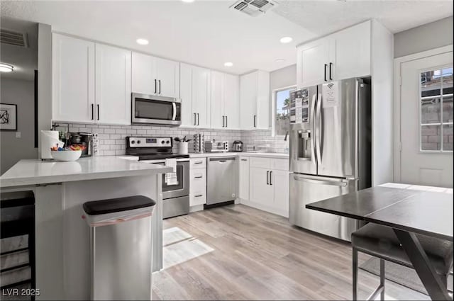 kitchen with white cabinets, appliances with stainless steel finishes, light wood-type flooring, and kitchen peninsula