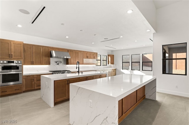 kitchen featuring sink, stainless steel appliances, a large island, and wall chimney range hood