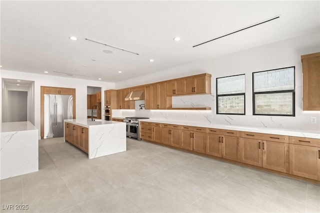 kitchen featuring a center island, wall chimney range hood, sink, light stone counters, and stainless steel appliances