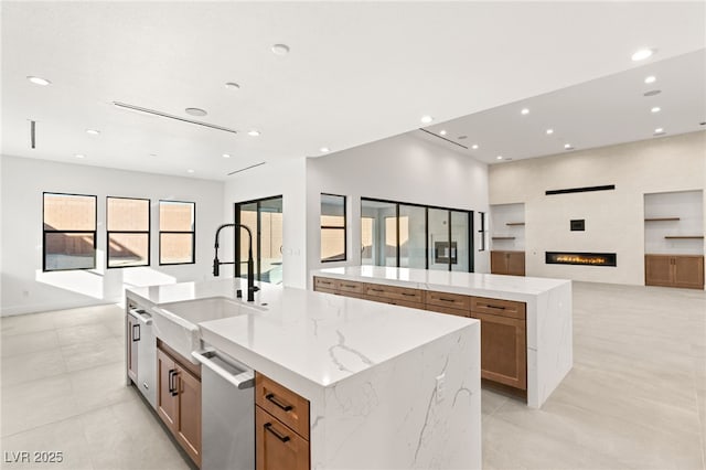 kitchen featuring stainless steel dishwasher, light stone counters, a spacious island, and sink