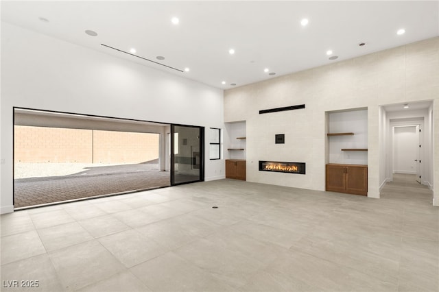 unfurnished living room featuring built in shelves, a towering ceiling, and a tiled fireplace