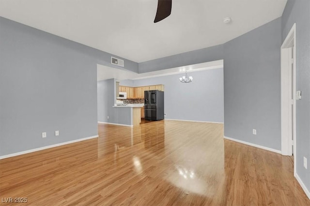 unfurnished living room with ceiling fan with notable chandelier and light hardwood / wood-style flooring