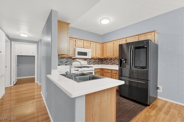 kitchen with sink, kitchen peninsula, light hardwood / wood-style floors, white appliances, and light brown cabinetry