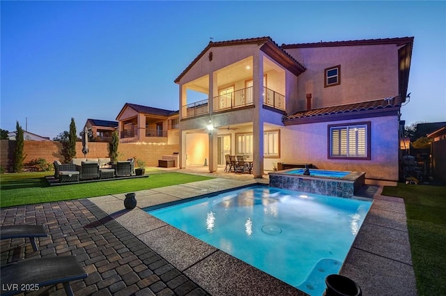 back house at dusk with a swimming pool with hot tub, ceiling fan, a balcony, an outdoor living space, and a patio