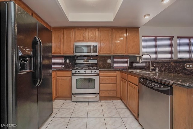 kitchen with dark stone counters, sink, light tile patterned floors, a tray ceiling, and stainless steel appliances