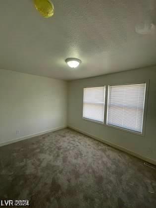 unfurnished room with dark colored carpet and a textured ceiling