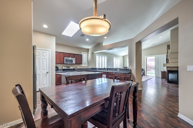 dining area with vaulted ceiling with skylight, dark hardwood / wood-style flooring, sink, and a stone fireplace