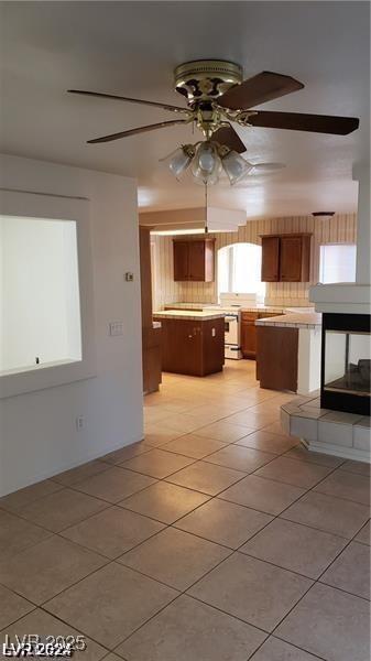 kitchen featuring ceiling fan, a kitchen island, light tile patterned floors, and backsplash