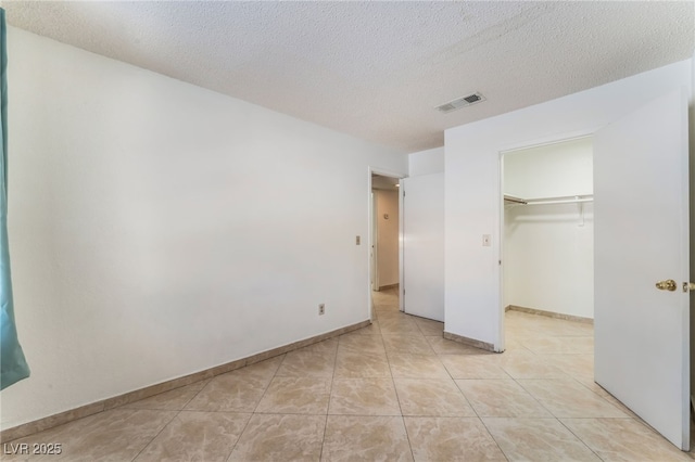 unfurnished bedroom with a walk in closet, a textured ceiling, light tile patterned floors, and a closet