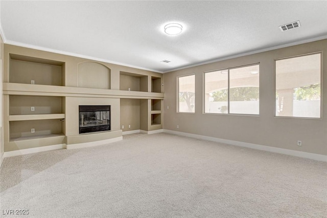 unfurnished living room with carpet flooring, built in shelves, a textured ceiling, and crown molding