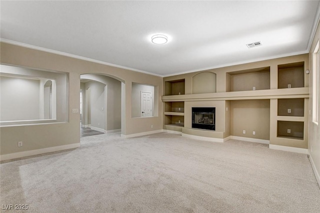 unfurnished living room featuring built in shelves, ornamental molding, and carpet floors