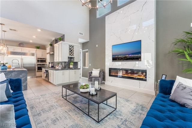 tiled living room with a premium fireplace, a towering ceiling, and a chandelier