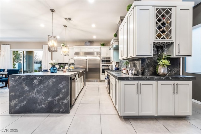 kitchen featuring wall chimney exhaust hood, pendant lighting, stainless steel appliances, decorative backsplash, and a kitchen island with sink