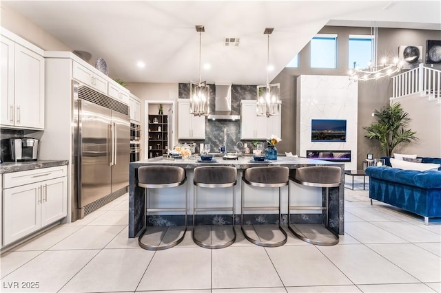 kitchen with wall chimney exhaust hood, decorative light fixtures, a kitchen bar, white cabinetry, and appliances with stainless steel finishes