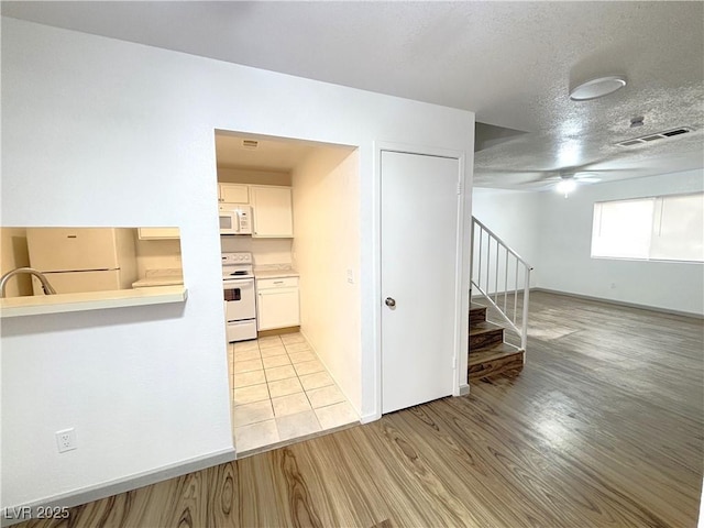 kitchen featuring a textured ceiling, white appliances, ceiling fan, light hardwood / wood-style flooring, and white cabinets