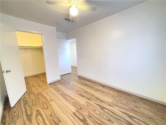 unfurnished bedroom featuring ceiling fan, a closet, light hardwood / wood-style floors, and a spacious closet