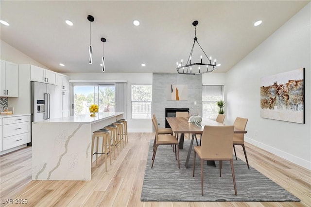 dining room featuring vaulted ceiling, a tiled fireplace, a notable chandelier, and light wood-type flooring