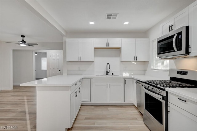 kitchen featuring sink, appliances with stainless steel finishes, kitchen peninsula, ceiling fan, and white cabinets