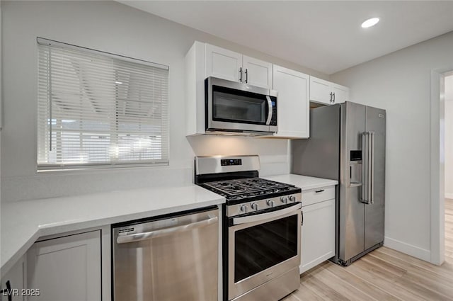 kitchen with appliances with stainless steel finishes, light wood-type flooring, and white cabinets